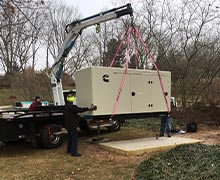 A Cummins commercial standby generator being lowered to an installation pad by crane