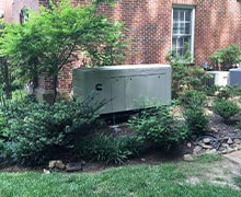 A large Cummins commercial standby generator installed neatly in the landscaping on the side of a red brick home