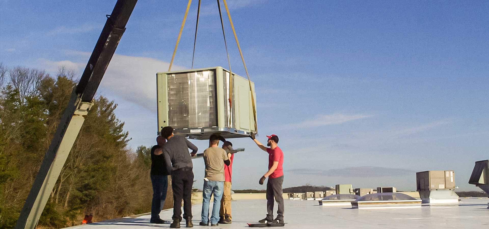 HVAC technicians guide a new heating and air unit hoisted by a crane towards a roof top installation site