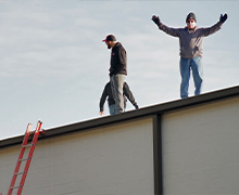 The Five Star Power Systems team up on the roof of a commercial building during an AC system installation. Five Star founder Ken Kloster has his arms raised in the air looking down at the camera.