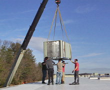 A new Rheem air conditioning unit being lowered by crane and guided by the team to the installation site